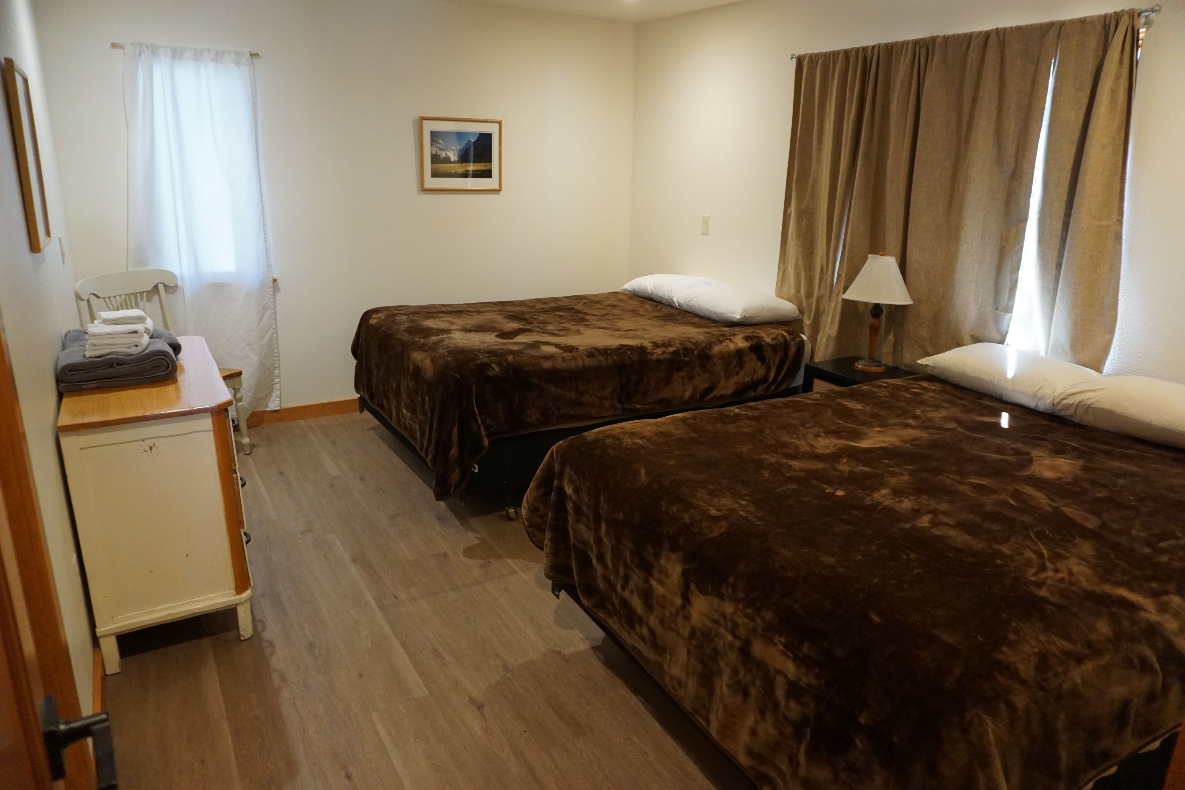A hotel room with two beds, a desk with a chair, a lamp, and a painting on the wall.