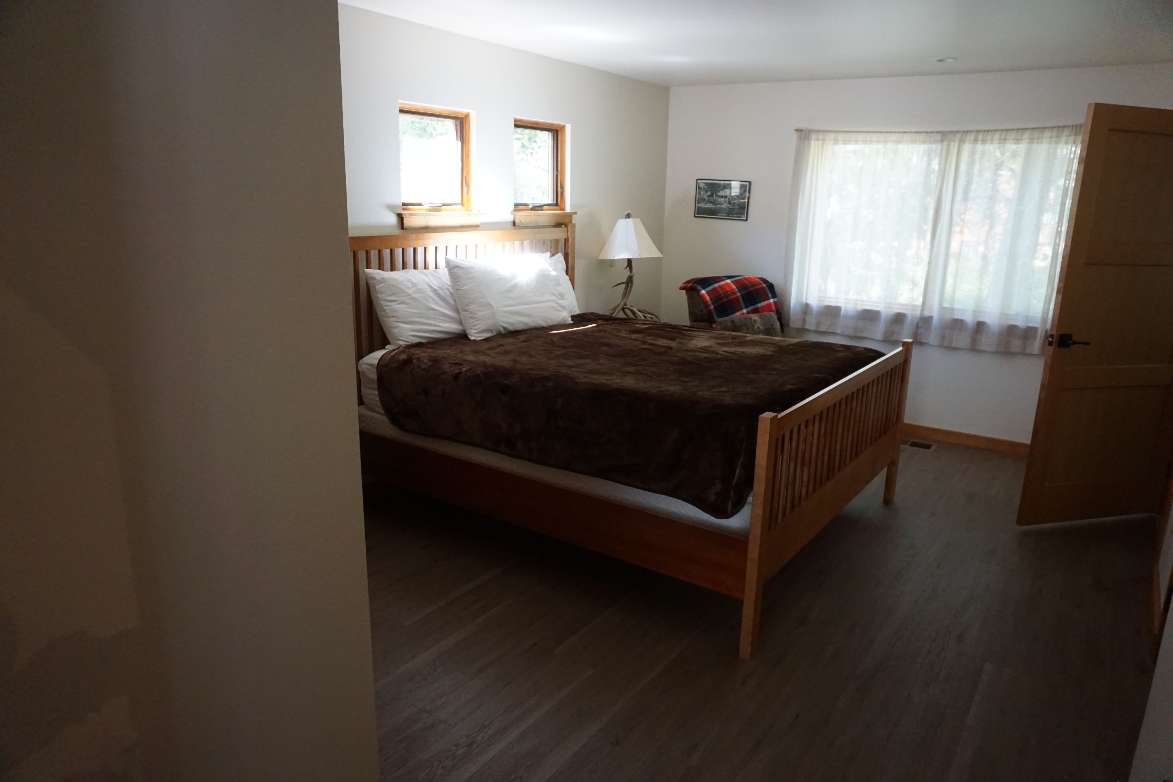 Ein Schlafzimmer mit einem hölzernen Bett, einem Nachttisch, einer Lampe, einem Sessel und einem Fenster mit Vorhängen.