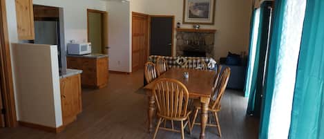 A spacious living area with a wooden dining table surrounded by chairs, a kitchen with a microwave, and a fireplace.
