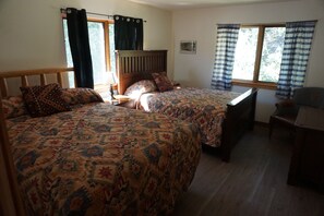 A double bed with patterned bedding, a wooden headboard, a nightstand, a desk, and a radiator.