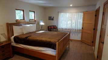 Ein Schlafzimmer mit einem hölzernen Bett, Nachttischen, einer Lampe, einem Sessel und einer Tür.