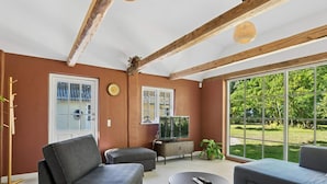 A living room with a sofa, ottoman, and a coffee table. There is a television and a plant on a stand. - 4 Star Holiday Home in Harpelunde (Harpelunde)