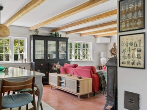 Ein Essbereich mit Tisch und Stühlen, eine schwarze Vitrine mit Glastüren, ein rotes Sofa und ein Kamin.