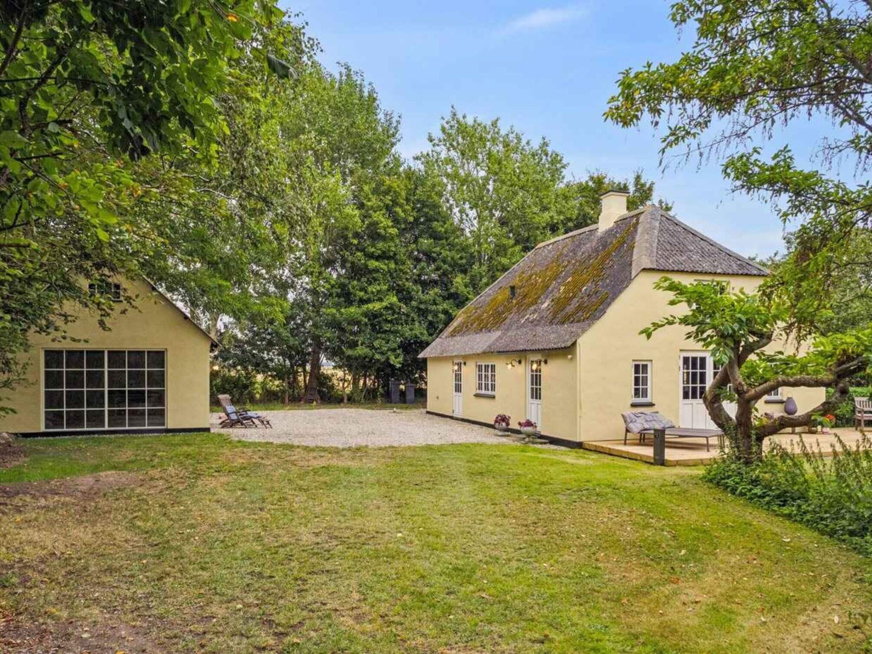 A house with a gravel driveway, a lawn, and a tree in the foreground.