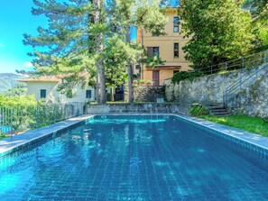 A swimming pool with a stone wall and a building with a balcony in the background. - Casa Ambra by Interhome (Nesso)