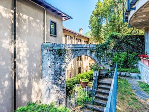 A stone bridge connecting buildings, a staircase with metal railings, and potted plants. - Casa Ambra by Interhome (Nesso)