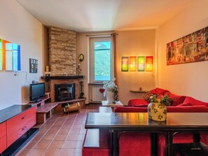 A living room with a fireplace, red sofa, and a table with a vase. - Casa Ambra by Interhome (Nesso)
