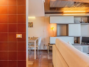 Ein modernes Wohnzimmer mit einer Couch, einem Esstisch mit Stühlen, einem Fernseher und einer Lampe.