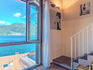 Ein Zimmer mit großem Fenster mit Blick auf ein Gewässer und einen Berg, einer Treppe und einer Wandleuchte.