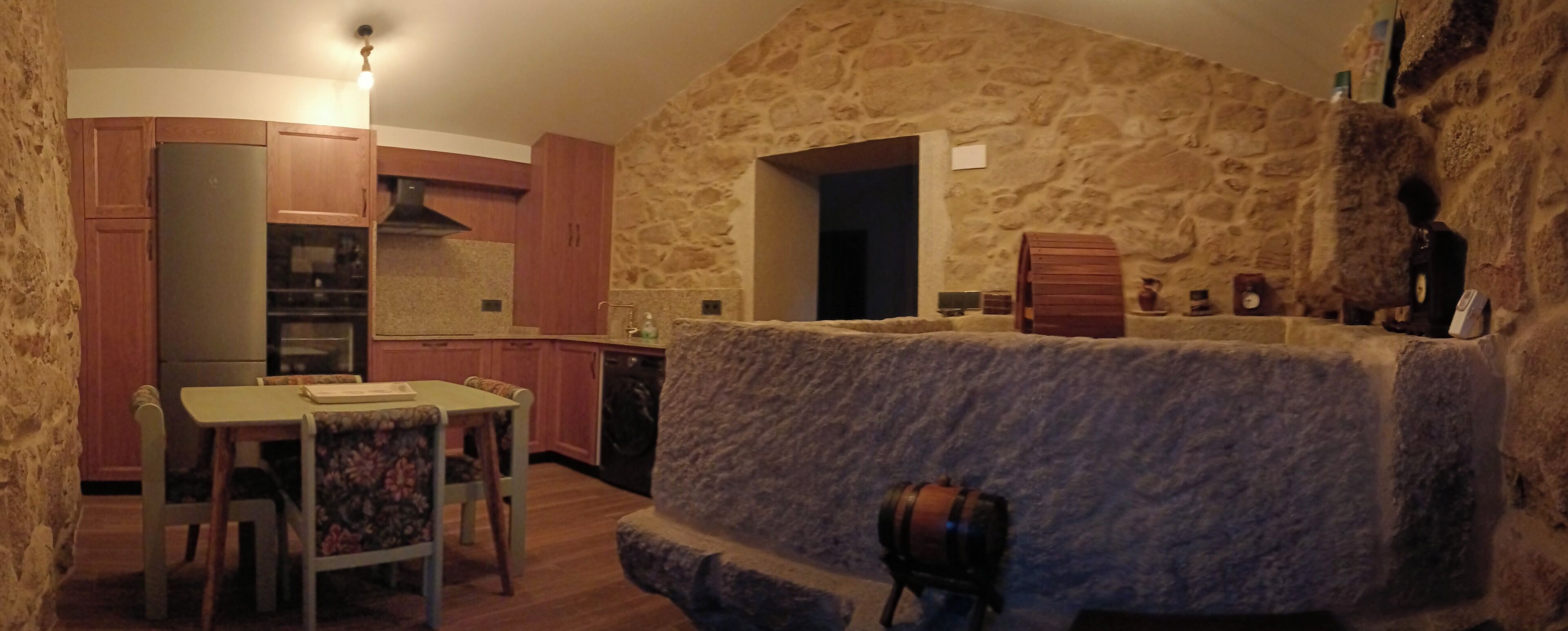 Een keuken met stenen muren, houten kasten, een eettafel met stoelen en een klein houten krukje.