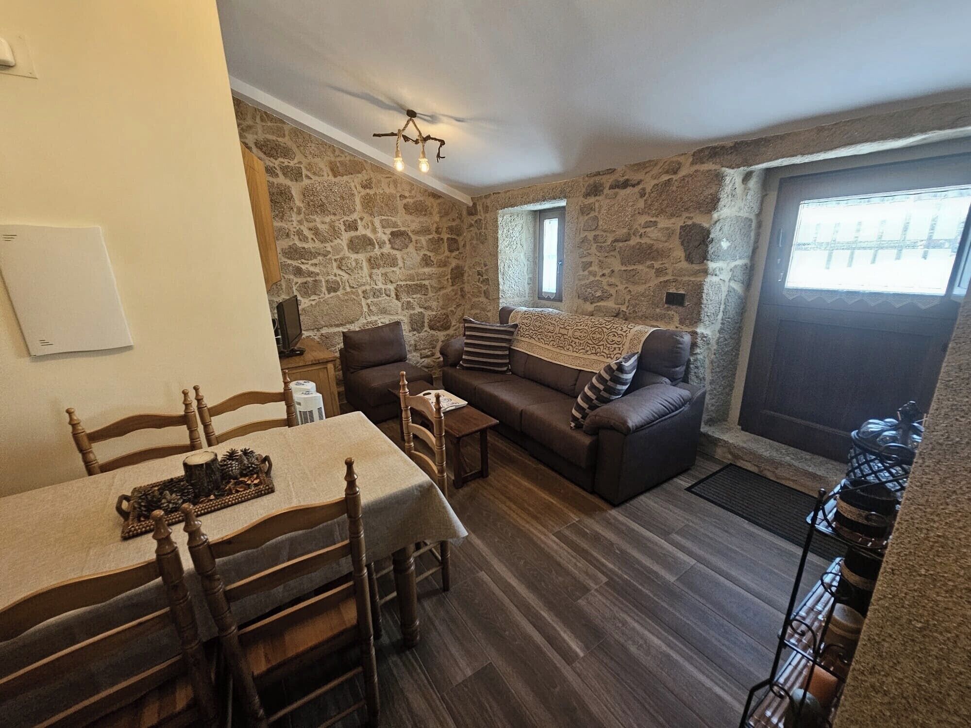 Una habitación acogedora con una pared de piedra, un sofá, una mesa de comedor con sillas y una ventana.