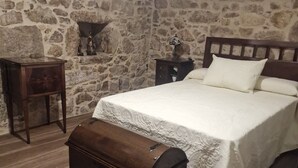 A bedroom with a stone wall, a wooden bed, a nightstand, a dresser, and a suitcase.