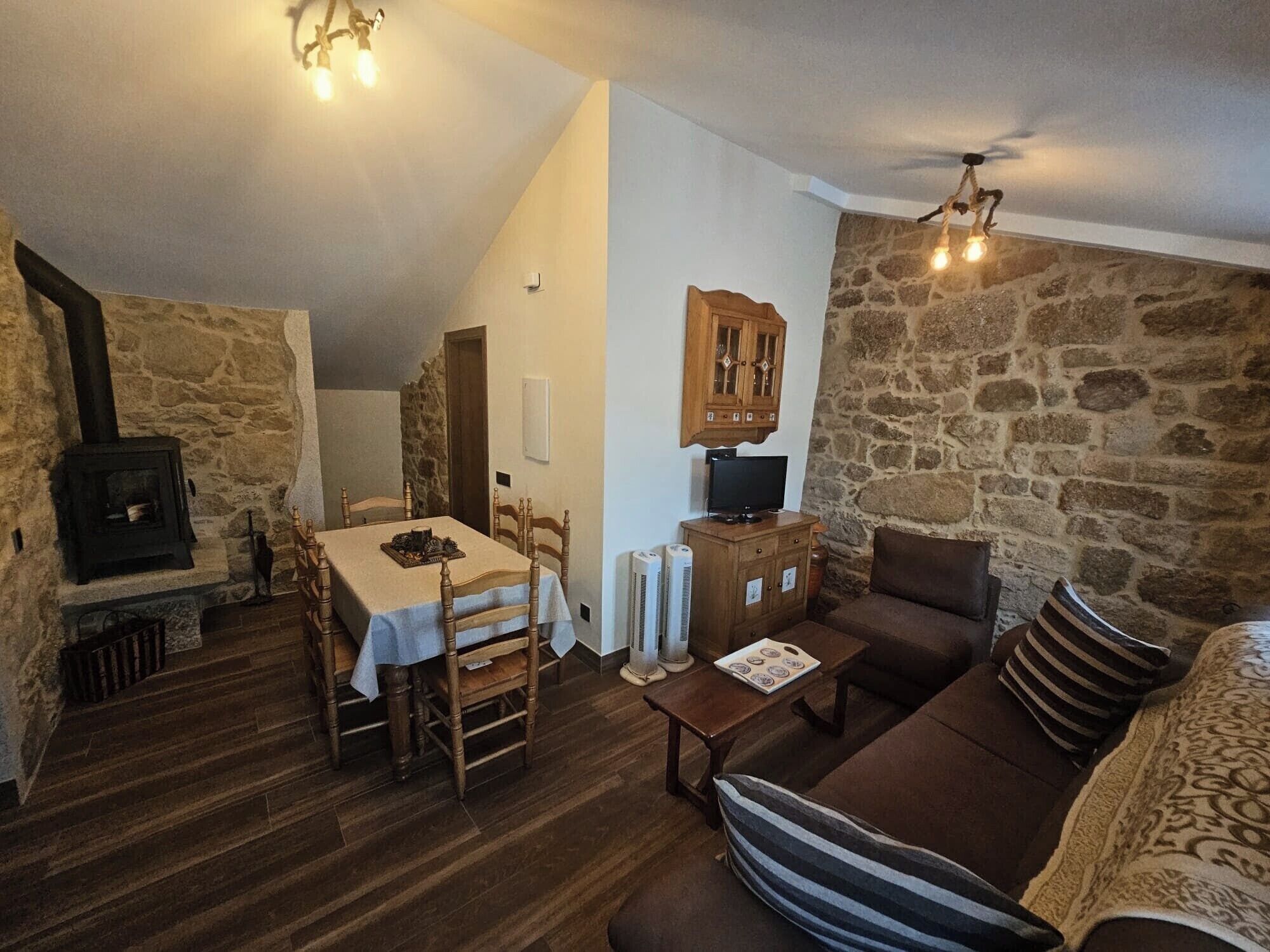 Una sala de estar acogedora con pared de piedra, chimenea, mesa de comedor con sillas, sofá y televisor.