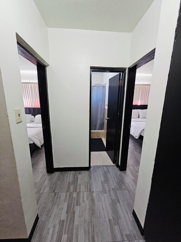 A hotel room with a bed, a bathroom with a shower curtain, and a hallway leading to another room.