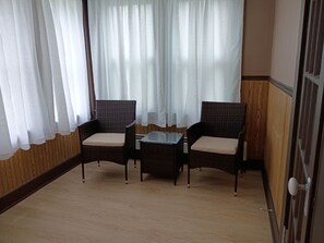 Ein Zimmer mit zwei KorbstĂŒhlen, einem kleinen Tisch und transparenten weiĂen VorhĂ€ngen.