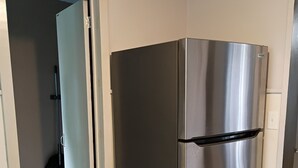 A stainless steel refrigerator in a kitchen with a tiled floor and a doorway leading to another room.