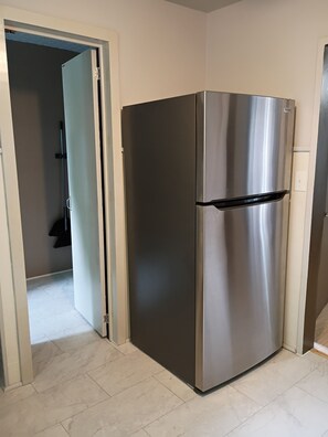 Ein Edelstahl-KĂŒhlschrank in einer KĂŒche mit Fliesenboden und einer TĂŒr zu einem anderen Raum.