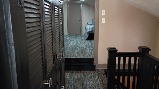 A staircase leading to a bedroom with a bed, a door with louvered shutters, and a carpeted floor.