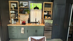 A modern kitchen with green cabinets, a stainless steel refrigerator, and a window with curtains. - Charming studio in the forest, fully equipped, 2.4 miles from Hiwassee River. (Decatur)