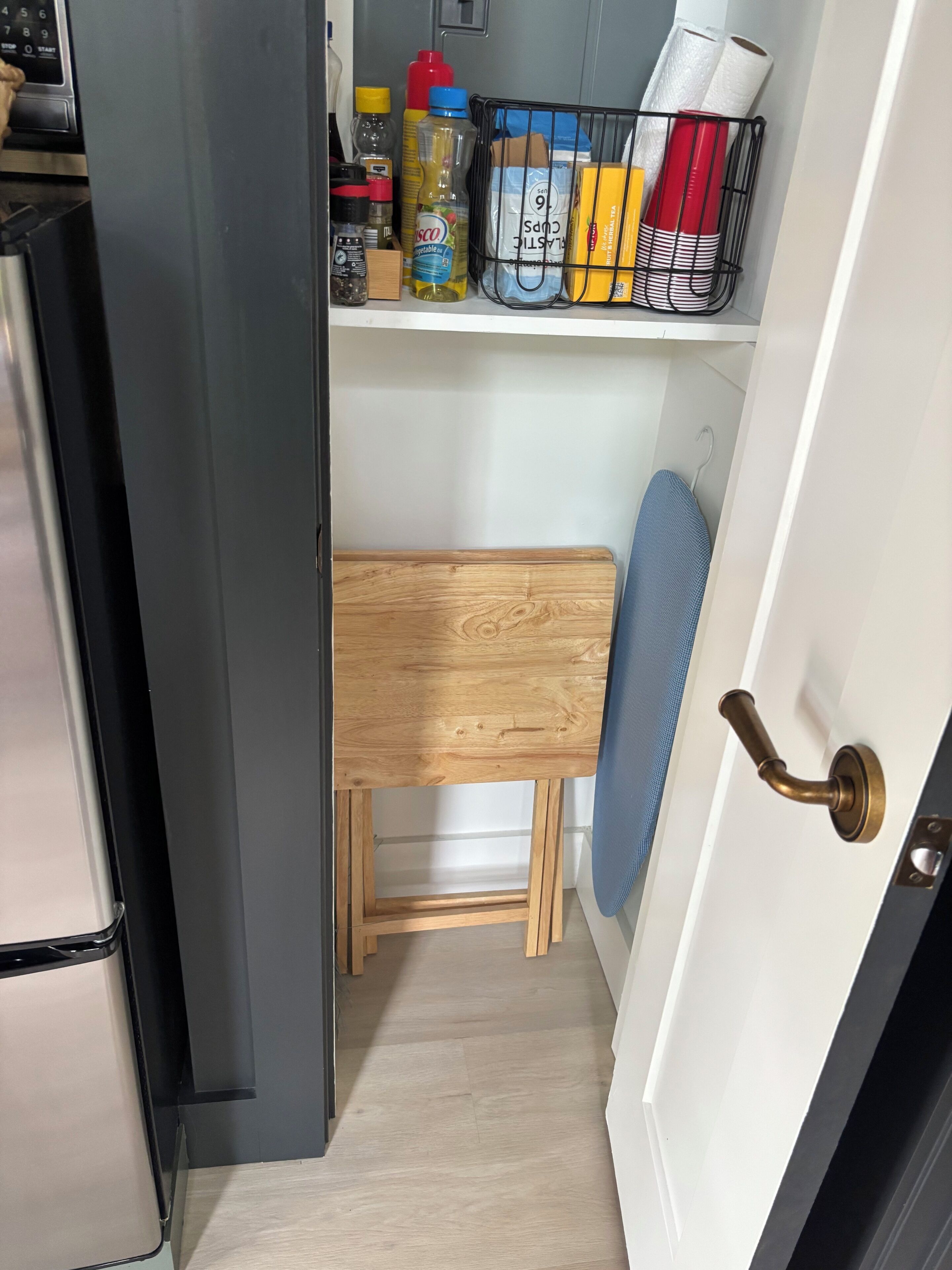Una cocina compacta con microondas integrado, un taburete de madera y una estantería metálica con utensilios básicos.