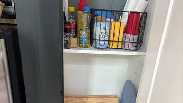 Una cocina compacta con microondas integrado, un taburete de madera y una estantería metálica con utensilios básicos.