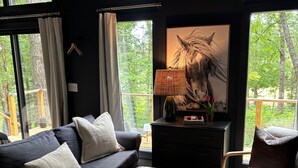 Un salon moderne avec un canapé, des fauteuils, un tapis et une grande fenêtre donnant sur la forêt.