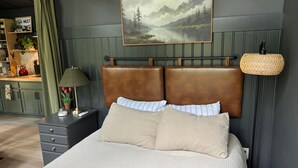 Une chambre à coucher avec un lit, une table de chevet, une lampe, un tableau et un abat-jour en osier.