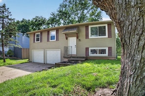 Ein zweigeschossiges Haus mit Garage, Veranda und einem Baum im Vordergrund.