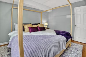 Una cama con dosel, un tablero de noche con lámpara y una alfombra estampada en el suelo.