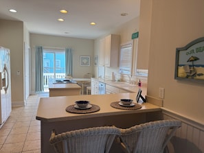 A kitchen with a dining area, a view to the outside, and a sign on the wall. - Ticket to Paradise at Holden Beach - Beach access just steps away! (Holden Beach)