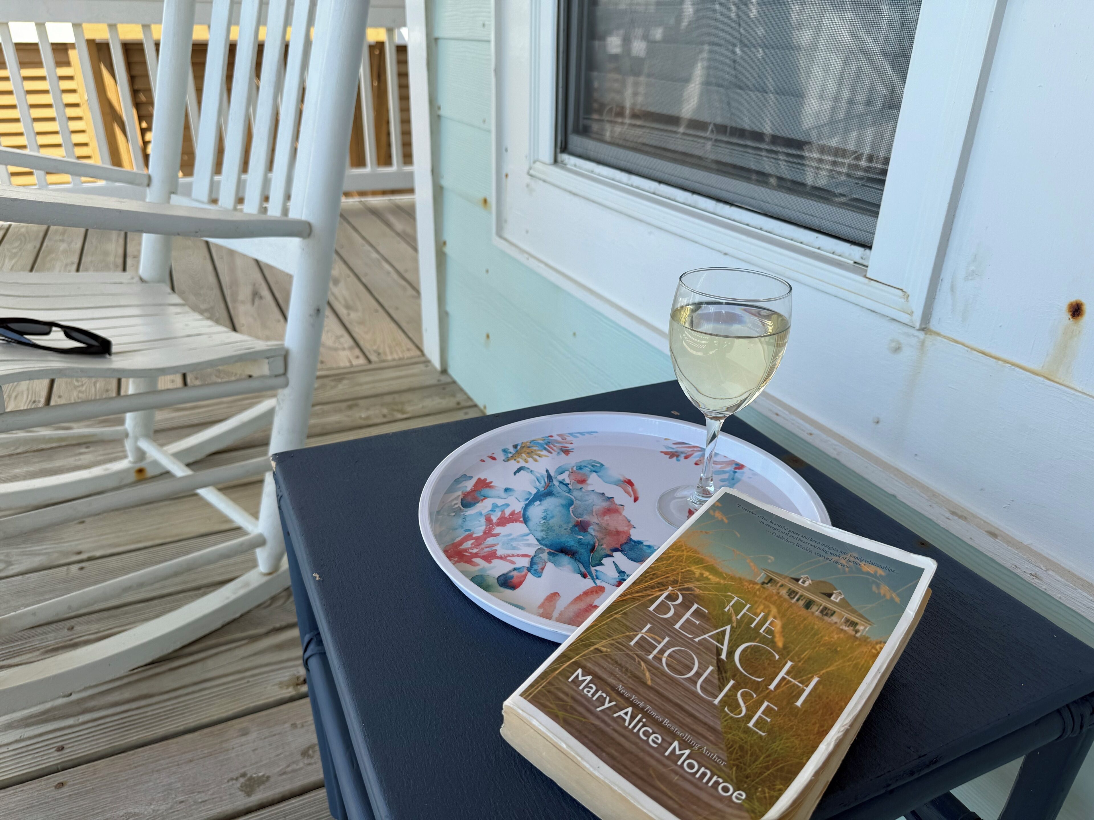 A book titled 'The Beach House' by Mary Alice Monroe on a table with a glass of white wine.