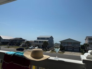 Ein Balkon mit einem Strohhut und einem Glas Wasser, mit Blick auf eine Straße mit Häusern und parkenden Autos.