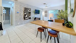 A modern kitchen with a wooden dining table, two stools, and a large decorative wall piece. - Chic Boho Paradise: Las Olas (Oakland Park)