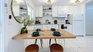 A modern kitchen with white cabinets, a wooden dining table, and two brown chairs. - Chic Boho Paradise: Las Olas (Oakland Park)