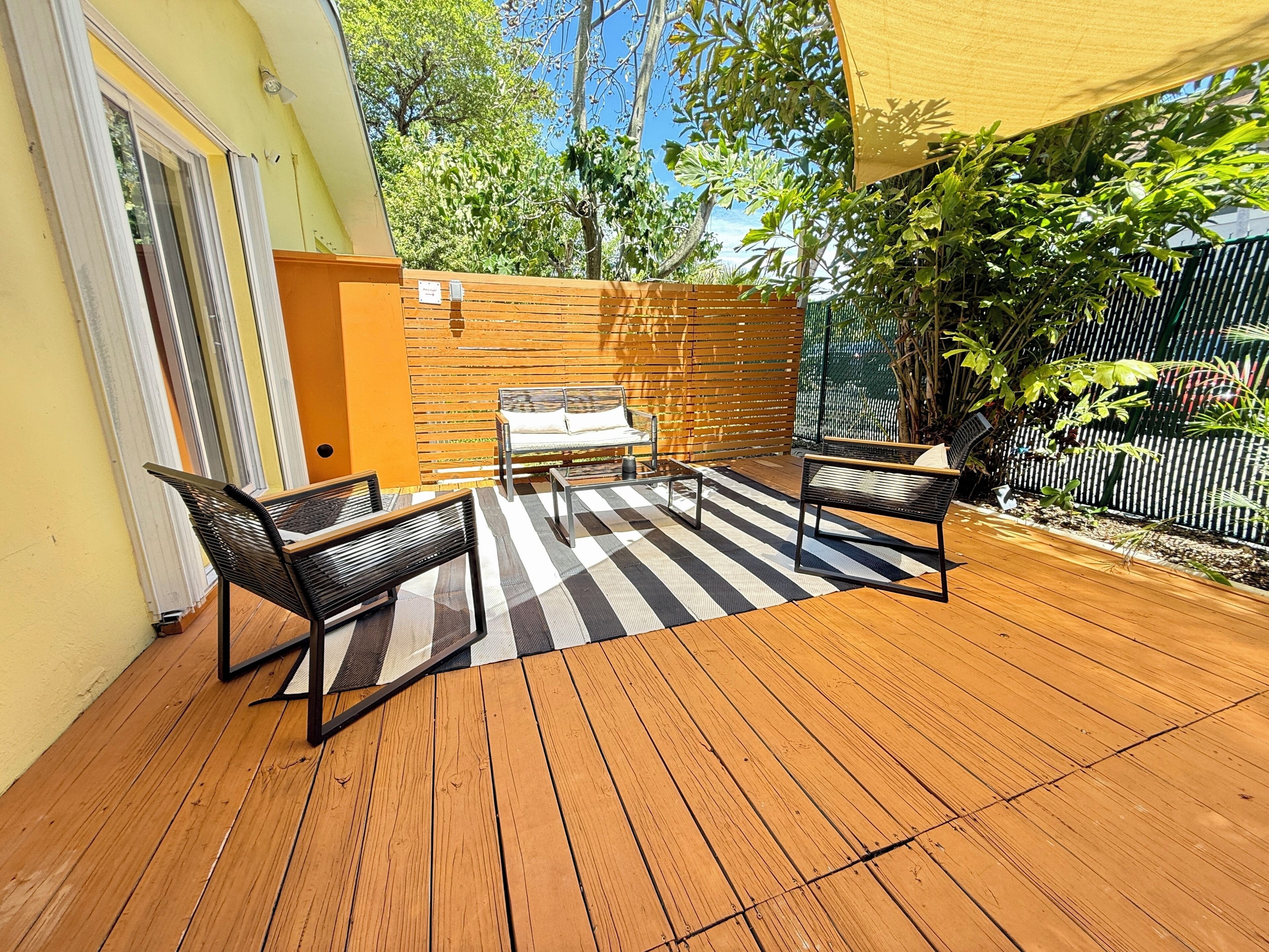 A wooden deck with a striped rug, two black metal chairs, and a bench.