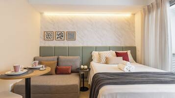 Quarto de hotel com cama, sofá, mesa pequena com xícara e pires, e parede com três quadros.