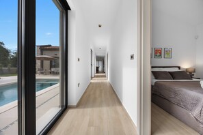 Ein modernes Hotelzimmer mit großem Fenster, einem Bett, einem Nachttisch und Blick auf den Pool.