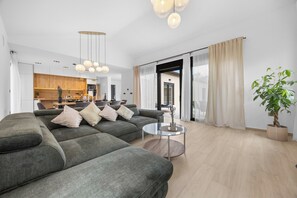 Ein modernes Wohnzimmer mit einem grauen Sofa, einem Glastisch und einem großen Fenster mit Vorhängen.