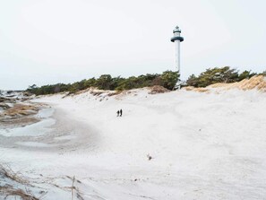 Un faro en una playa arenosa con vegetación escasa.
