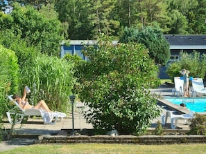Zona de piscina con sillones de descanso, piscina y un edificio al fondo.