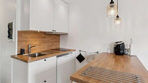 Ett modernt kök med vita skåp, en bänkskiva i trä, en inbyggd diskmaskin och en vattenkokare.
