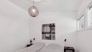 Ett minimalistiskt sovrum med en säng, sängbord, en hängande lampa och ett konstverk på väggen.
