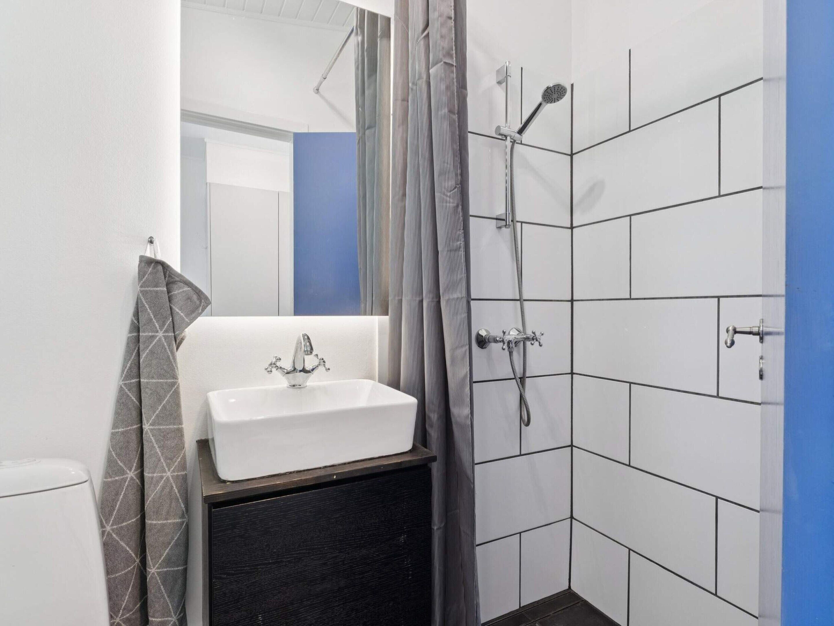 A bathroom with a white sink, a shower with a handheld showerhead, and a towel hanging on a rack.