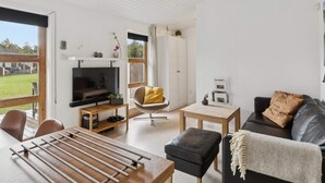 Ett modernt vardagsrum med TV, soffa, matbord och utsikt över omgivningarna.
