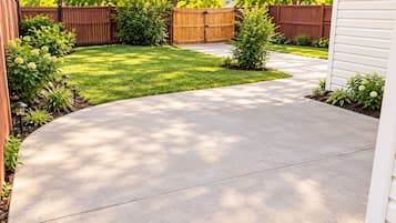 A curved concrete driveway leading to a wooden fence and a grassy yard.