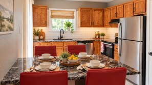 Una cocina con armarios de madera, un refrigerador de acero inoxidable y un comedor con sillas rojas y encimera de mármol.