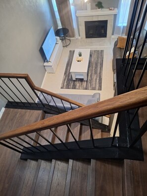 A staircase with wooden handrails and black metal supports, leading to a living room with a fireplace, a TV, and a coffee table. - 4BR/3BT Spacious Family Retreat,Quick Access to Downtown perfect for Group Stays (Dallas)