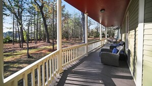 A covered porch with a railing, outdoor furniture, and a view of a wooded area. - Two Dining Tables · Sleeps 14 · 7BR, 4 Baths (Fuquay-Varina)
