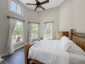 Ein Schlafzimmer mit einem Bett, einem Deckenventilator und drei Fenstern mit Vorhängen.