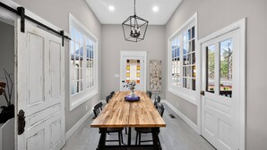 A dining room with a wooden table, chairs, and a hanging light fixture. - Two Dining Tables · Sleeps 14 · 7BR, 4 Baths (Fuquay-Varina)